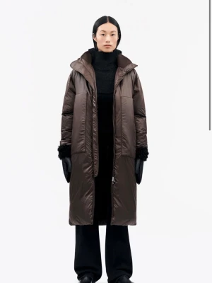 Brun lång pufferjacka Tiger of Sweden - Helt ny lång, brun pufferjacka med huva och raka linjer. Jackan har totalt fyra fickor framtill, dragkedja hela vägen och bekväma muddar detaljer vid ärmsluten, även samma mudd material vid kragen vilket är super bekvämt och varmt! Perfekt för kalla dagar och ger en clean, oversized vibe då den är lite större i storleken☺️Nypris:799euro/87050sek!