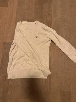 Vit kabelstickad tröja från Gant XS - Kabelstickad vit tröja från Gant i storlek XS. Klassisk rund halsringning, broderad Gant-logga med sköld på bröstet och ribbade muddar. Perfekt för lager-på-lager.