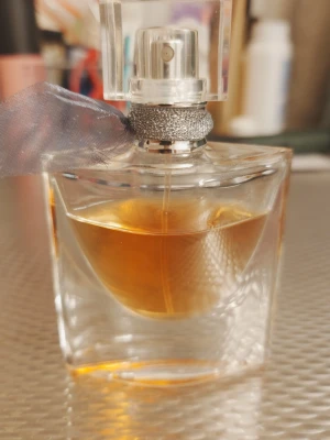 Elegant parfym med rosett - Snygg och stilren parfymflaska från Lancome med en dekorativ rosett runt halsen. Perfekt för dig som vill ha en lyxig touch i din samling. Volym och ingredienser syns ej på bilden.