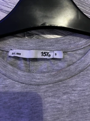Grå långärmad topp från 157 - En basic grå långärmad topp från 157 med rund halsringning. Modellen är croppad och har en enkel, stilren look som passar till allt. Tillverkad i mjukt material som känns skönt mot huden. Perfekt att matcha med jeans eller kjol. köpt för 200, nästan aldrig andvänd 
