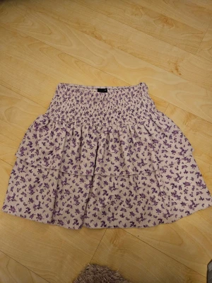 Supergullig ljuslila blommig kjol Gina Tricot XS - Jag säljer en supersöt kort sommarkjol från Gina Tricot i storlek XS. Kjolen är ljuslila med små lila blommor, har smockad midja och volangdetaljer som ger en skön och flowy känsla. Den är en perfekt volangkjol till sommaren, att matcha till söta toppar. Nypris runt 300 kr. I mycket bra skick, aldrig använd och därför priset.