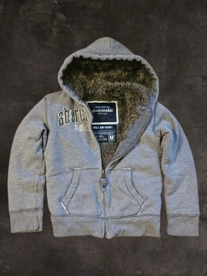 RARE Vintage Abercrombie and Fitch Wolf Jaw Jacket Hoodie Archive Fur Grisch Y2K Niche - This is the highly sought-after, vintage Abercrombie & Fitch "Wolf Jaw Jacket."  Ultimate Warmth: Fully lined with thick, luxurious faux fur (including the hood). Incredibly durable and cozy.  Quality: Heavy construction from the sought-after "Archive" A&F era.  Look: Faded grey with classic embroidered logo-great Y2K/vintage style.  IMPORTANT!!!  Fit Note: Label says M, but it runs very small and fits like a modern S-XS.  Grab a rare piece of A&F history!