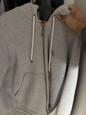 Burberry  grå hoodie  - Säljer en stilren grå burberry hoodie i storlek S. Klassisk modell med dragkedja, huva med snören och fickor framtill. Mjuk och skön i materialet, passar perfekt till vardags eller som ett extra lager. Hoodien är i bra skick och sparsamt använd. Enkel att matcha med både jeans och träningsbyxor !!! Om du vill byta med något gärna skriv till mig