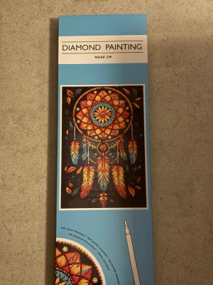 Diamond painting drömfångare 40x60 cm - Diamond painting-kit med motiv av en färgglad drömfångare i orange, blått och gult. Innehåller strasstenar, penna, sorteringsbricka, silikonvax och mönsterark. Perfekt för dig som gillar pyssel och vill skapa en unik tavla.