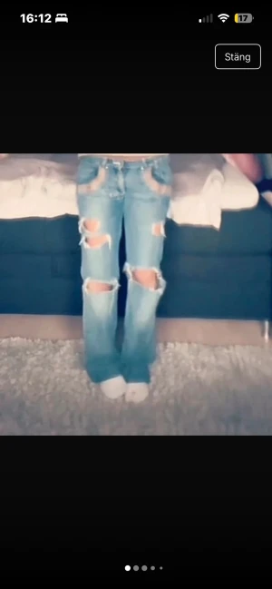 lågmidjade bootcut jeans med hål - Säljer ett par blå jeans från AJ Jeans med stora, trasiga hål på benen och coola slitningar. Byxorna har raka ben, klassiska fickor och beige detaljer vid fickorna. Perfekt för dig som gillar en edgy och avslappnad stil. ja är 165 o de passar mig perfekt i längden men tror inte dom skulle passa nån över 170
