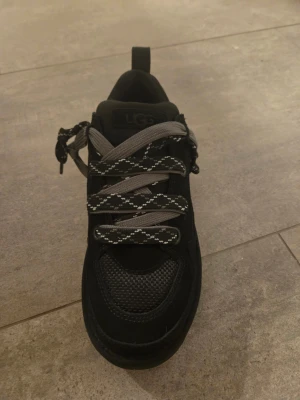 Svarta UGG sneakers Lowmel - Snygga svarta sneakers från UGG. Skorna har både mesh och mockadetaljer, samt grå och svartmönstrade snören med vita inslag. Perfekt för dig som gillar streetstyle och vill ha något som sticker ut.