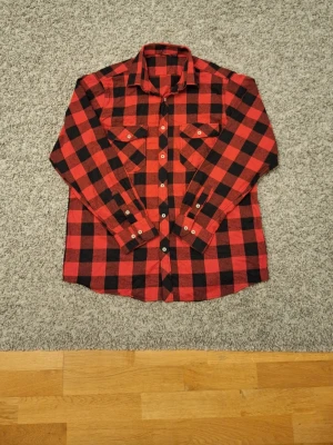 Röd och svart rutig flanell skjorta - Klassisk röd och svart rutig flanell skjorta i storlek L(passar M också). Använd fåtal gånger och skicket är jättebra, inga slitningar eller defekter finns. Skjortan har två bröstfickor samt krage och ärmar. Skick: 8/10