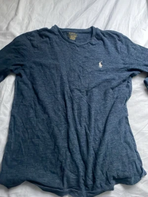 Blå långärmad t-shirt Polo Ralph Lauren - Snygg blå långärmad t-shirt från Polo Ralph Lauren i custom slim fit. T-shirten har en klassisk rund hals och den ikoniska vita Polo-loggan broderad på bröstet. Materialet är mjuk bomull som känns skönt mot huden. Perfekt för en chill och stilren look.