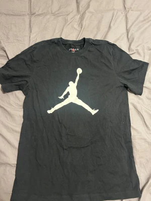 Svart Jordan t-shirt med logga - Svart t-shirt från Jordan med den ikoniska Jumpman-loggan i vitt på bröstet. Klassisk rund hals och korta ärmar. Tillverkad i mjuk bomull och har en normal passform som sitter skönt på kroppen.