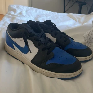 Nike Air Jordan 1 Low blå/svart/vit - Säljer ett par Nike Air Jordan 1 Low i blått, svart och vitt skinn. Klassisk siluett med svart snörning, blå detaljer på tå och häl samt vit mellansula. Ikonisk Air Jordan-logga broderad på hälen. Perfekta för dig som vill sticka ut med en tidlös sneaker. Och dem är knappt använda och är skit snygga sänker vid snabb affär
