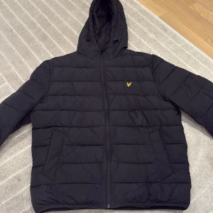 Svart pufferjacka från Lyle & Scott - Säljer en svart pufferjacka från Lyle & Scott i storlek L. Jackan har huva, dragkedja framtill. Perfekt för kyliga dagar och riktigt skön att bära. Jackan är vadderad och har två fickor på sidorna. Nypris:2000kr använd en vinter