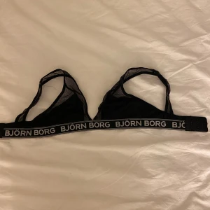 Svart mesh linnetopp från Björn Borg - Sportig svart linnetopp från Björn Borg med meshdetaljer och bred resår med logotyp. Toppen är ärmlös och har en stilren, tight passform, aldrig använt