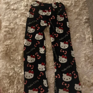 Hello Kitty mjukisbyxor svart - Mysiga svarta mjukisbyxor med Hello Kitty-motiv och rosa rosetter över hela byxorna. 