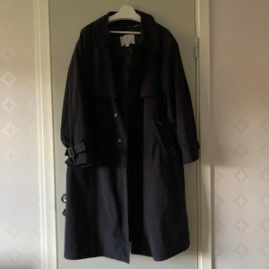 Svart trenchcoat från London Fog - Klassisk svart trenchcoat från London Fog med knappar framtill och snygga spänndetaljer vid ärmsluten. Jackan har en rak passform, krage och djupa fickor. Storlek uppskattas till L, men sitter rätt oversized. Perfekt för dig som gillar stilrena och tidlösa plagg. Dessutom har den fodring som går att ta bort om man vill ha en lite svalare jacka på lite varmare dagar. Säljer för 400 kr + frakt (köpare står för frakt) 💕