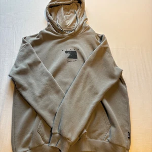 Ljusgrå hoodie från Zigh med print - Snygg beige hoodie från Zigh med svart grafiskt print på både bröstet och ryggen. Tröjan har huva, känguruficka och ribbade muddar. Perfekt för dig som gillar streetwear och vill ha en stilren look med coola detaljer.