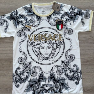  Puma fotbollströja M - Unik vit fotbollströja med detaljerat barockmönster i svart och grått samt Italiens landslagsemblem på bröstet. Guld Puma-logga och gul dekor runt kragen. Materialet är lätt och andas, perfekt för match eller streetwear.