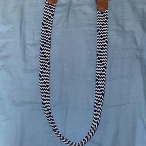 Randigt blåvitt bälte med skinnspänne - Snyggt bälte med blåvitt zickzackmönster och detaljer i brunt skinn. Bältet är i nytt skick . Den är 95cm med stretch