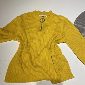 Gul ribbad tröja med dragkedja H&M - Gul ribbad långärmad tröja från H&M med cool ringformad dragkedja framtill. Tröjan har en högre hals och är tillverkad i mjuk bomullsmix. Perfekt för dig som vill sticka ut med färg och stil.