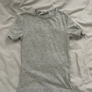 Grå basic thight t-shirt från weekday - Enkel och stilren grå t-shirt från weekday i mjuk bomull. T-shirten har korta ärmar, rund halsringning och en lätt melerad look. Perfekt för en chill och avslappnad stil. Thight!