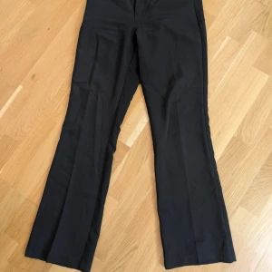 Svarta kostymbyxor från Bik Bok - Svarta kostymbyxor från Bik Bok i klassisk modell med raka ben och diskret dragkedja fram. Byxorna har två bakfickor och är tillverkade i ett mjukt tyg som ger en snygg passform. Perfekta för en stilren look.