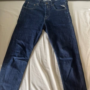 Mörkblå jeans från Replay, Tinmar Tapered - Säljer ett par mörkblå jeans från Replay med storlek W28 L32 och klassisk femficksdesign och kontrastsömmar. Jeansen har rak passform och normal midja, tillverkade i slitstarkt denimtyg. Snygga detaljer på bakfickorna och Replay-logga vid myntfickan.