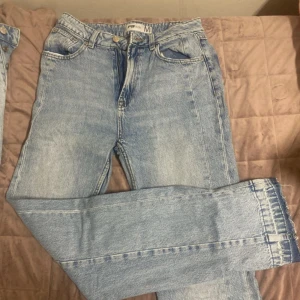 Ljusblå jeans med råa kanter - Säljer ett par ljusblå jeans från Fifth Season i klassisk femficksmodell. Jeansen har hög midja, raka ben och råa, fransiga benslut för en trendig look. Tillverkade i jeansmaterial med dragkedja och knapp framtill.