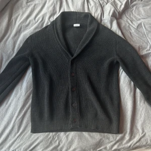 Svart ribbad kofta från John Henric - Säljer en svart ribbstickad kofta från John Henric. Koftan har snygg sjalkrage, knäppning med fyra knappar framtill och är långärmad. Perfekt för lager-på-lager och chill stil. Materialet är mjukt och stickat för extra komfort.