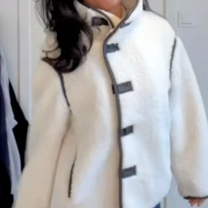 Vit teddyjacka med svarta detaljer - Säljer en supermysig vit teddyjacka med svarta detaljer och snygga knäppningar framtill. Jackan har hög krage, markerade svarta sömmar och är perfekt för kyliga dagar. De första bilderna är lånade.