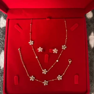 Guldigt smyckeset med blommor - Snyggt smyckeset med halsband, armband och örhängen i rostfritt stål .Perfekt för dig som gillar detaljer och blommiga smycken. Lådan följer inte med