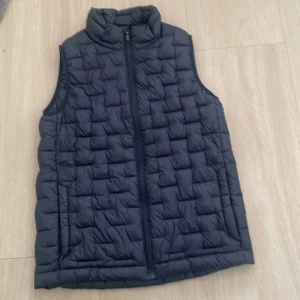 Svart dunväst från Everest - Svart quiltad dunväst från Everest med hög krage och dragkedja framtill. Västen har en stilren look och är perfekt för lager-på-lager. Lätt och smidig att bära, passar till många outfits.