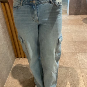 Ljusblå cargojeans från Lindex - Säljer ett par ljusblå cargojeans från Lindex med breda ben och stora fickor på sidorna. Jeansen har normal midja, raka ben och klassisk jeansknäppning. Perfekta för dig som gillar en avslappnad och trendig stil.