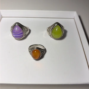 Tre vintageinspirerade silverringar - Tre snygga silverringar med stora stenar i lila, grön och orange. Ringarna har detaljerade mönster runt infattningen och stenar i dropp- och ovalform. Perfekt för dig som vill sticka ut med färgglada accessoarer.