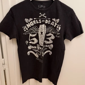Mörkgrå t-shirt Levi's med tryck - Mörkgrå t-shirt från Levi's med stort vitt tryck framtill med text, vingar och siffror. Klassisk rund hals och korta ärmar. Tillverkad i 100% bomull för en skön känsla. Perfekt för dig som gillar en edgy och cool stil. Storlek M.
