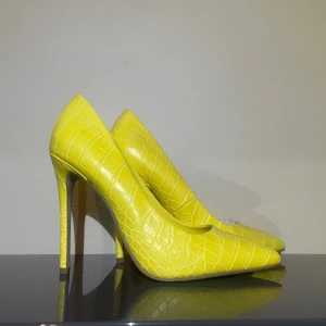 Gula pumps med krokodilmönster - ✨ Statement-klackar i krokopräglat gult – för dig som vågar sticka ut! ✨ 👠 Detaljer: 	•	Material: Krokopräglat konstläder med glansig finish 	•	Klackhöjd: Ca 10–12 cm – ger en smickrande hållning 	•	Modell: Spetsig tå för en elegant siluett 	•	Sula: Ljus med lätt grepp   💛Passar perfekt till: En stilren kostym, jeans med vit skjorta, eller din favoritklänning när du vill addera en färgklick och självförtroende.  Våga ta plats – dessa klackar är allt du behöver för att förvandla en enkel outfit 