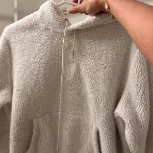 Vit fleecehoodie från Polo Ralph Lauren - Supermjuk och fluffig vit hoodie från Polo Ralph Lauren i teddyfleece. Tröjan har huva med snörning, känguruficka och broderad logga framtill. Perfekt för kyliga dagar när du vill vara både varm och snygg.