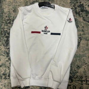 Vit sweatshirt från Moncler S - Vit sweatshirt från Moncler med broderad logga och Paris-text på bröstet samt patch på ärmen. Tröjan har rund hals, ribbade muddar och detaljer i rött, vitt och marinblått. Tillverkad i mjuk bomull för en clean och stilren look. Om ni har frågor då det är bara o ställa de😊