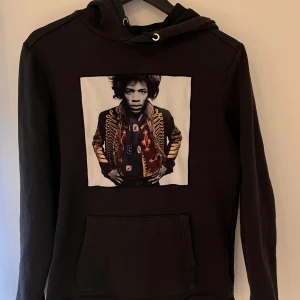 Limitato hoodie - Svart hoodie med stor ficka framtill och coolt tryck av en person i militärinspirerad jacka på bröstet. Tröjan har huva med snörning och långa ärmar. Perfekt för dig som gillar streetstyle och unika plagg.