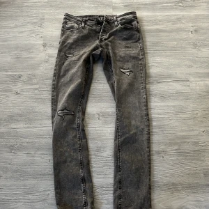 Grå slitna jeans Jack & Jones Slim Glenn - Säljer ett par grå jeans från Jack & Jones, modell Slim Glenn. Jeansen har slitna detaljer och hål på benen för en cool, trendig look. De är i slim fit och har klassisk femficksdesign. Perfekta för dig som gillar streetstyle.