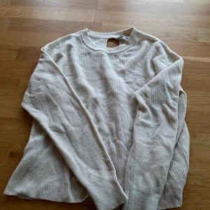 Beige ribbad tröja med twistad rygg  - Säljer en beige ribbad långärmad tröja från Mango. Tröjan har en twistad detalj och öppning i ryggen. 