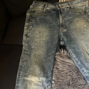 G-Star Raw jeans med slitningar strl 34 - ett par ljusblå jeans från G-Star med slitna detaljer. Jeansen har en rak passform och tydliga kontrastsömmar. Märkets logga syns på bakfickan och vid framsidan. 