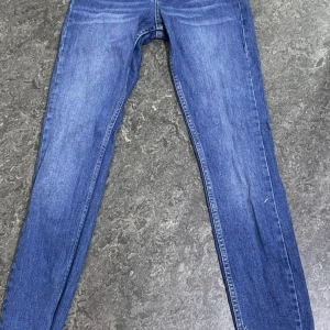 Blå skinny jeans från Perfect Jeans - Säljer ett par blå skinny jeans från Perfect Jeans i storlek 34. Jeansen har hög midja, knäppning med knappar och klassiska fem fickor. Materialet är jeans med lite stretch och benen avslutas med råa, fransiga kanter för en trendig look.