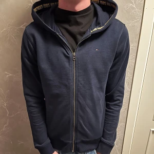 Tommy Hilfiger hoodie - Säljer en mörkblå Tommy Hilfiger hoodie i storlek 176cm men passar bra till 180cm.  Använd men fortfarande i ett väldigt bra skick. Nypris: ca 750kr  modell 183cm
