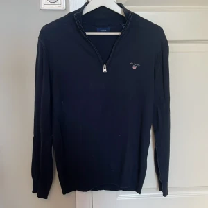 Marinblå half zip-tröja från GANT - Snygg marinblå långärmad tröja från GANT med half zip och liten broderad logga på bröstet. Tröjan har en klassisk passform och är tillverkad i mjuk bomull, perfekt för lager-på-lager-stil under höst och vinter. 