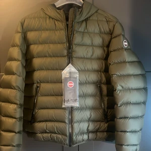 Olivgrön pufferjacka från Colmar - Snygg olivgrön pufferjacka från Colmar med rundad hals och två praktiska sidofickor med dragkedja. Jackan har ett stilrent, quiltat mönster och Colmar-logga på ärmen. Perfekt för dig som vill ha en varm och trendig look under kyliga dagar.