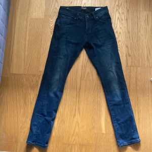 Mörkblå slim jeans Jack & Jones - Snygga mörkblå jeans från Jack & Jones, modell Slim/Glenn. Jeansen har klassisk femficksdesign, smal passform och är tillverkade i stretchig denim för extra komfort. Perfekta för dig som gillar en modern och stilren look. Storleken är 28/30. 