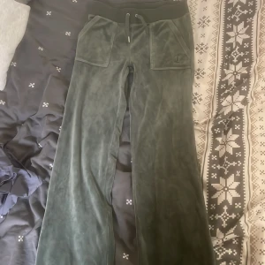 Gröna velourbyxor Juicy Couture XS - Mörkgröna mjukisbyxor från Juicy Couture i velour med bred resår och snörning i midjan. Byxorna har stora fickor fram och bak med knappar, samt broderad logga på ena fickan. Har en fläck som går bort i tvätten 