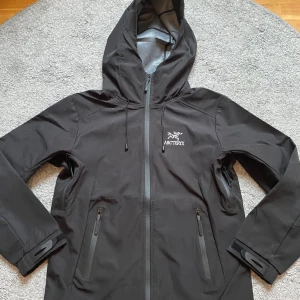 Svart vindjacka från Arc'teryx - Svart vindjacka från Arc'teryx med huva, justerbara ärmslut med kardborre och två dragkedjeförsedda fickor framtill. Jackan är bara andvänd ett fåtal gånger. Priset är förhandlingsbart! Hör av dig vid frågor.