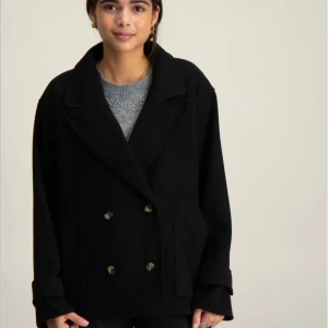 Svart skepparkavaj med knappar - Säljer en svart skepparkavaj med dubbelknäppning och bred krage. Jackan har stora fickor framtill och långa ärmar med dekorativa knappar vid mudden. Perfekt för dig som gillar en chill och klassisk stil med lite edge.