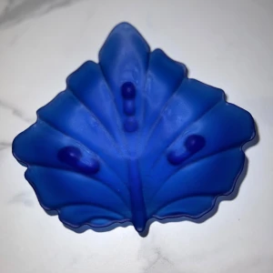 Lyxig Prydnadskål - Detta är en blå glasskål i form av ett löv. Skålen har en matt finish och dekorativa detaljer. Perfekt som dekoration eller för servering av snacks och godis. Inga synliga defekter eller slitage. Unik och stilren design som passar i de flesta hem.