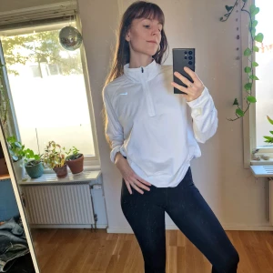 Vit Nike Dri-Fit långärmad träningströja - Klarvit långärmad träningströja från Nike med Dri-Fit-teknologi. Tröjan har halv dragkedja framtill, hög krage och diskret Nike-logga på bröstet. Perfekt för löpning eller gym. Materialet är lätt och andas, vilket gör den skön att ha på sig under träning men också i vardagen. Storlek XL